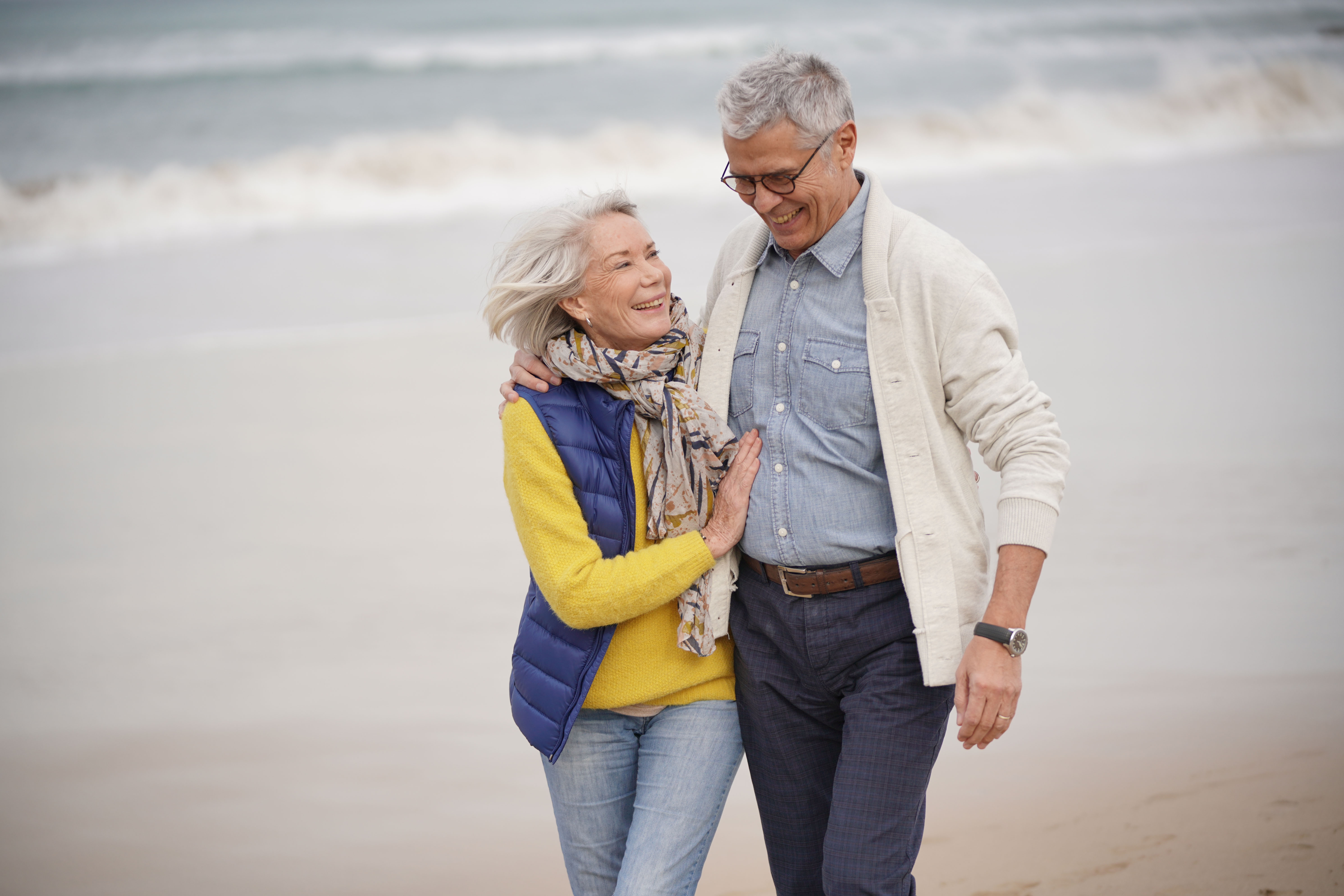 Older couple walking on beach with arms around onanother
