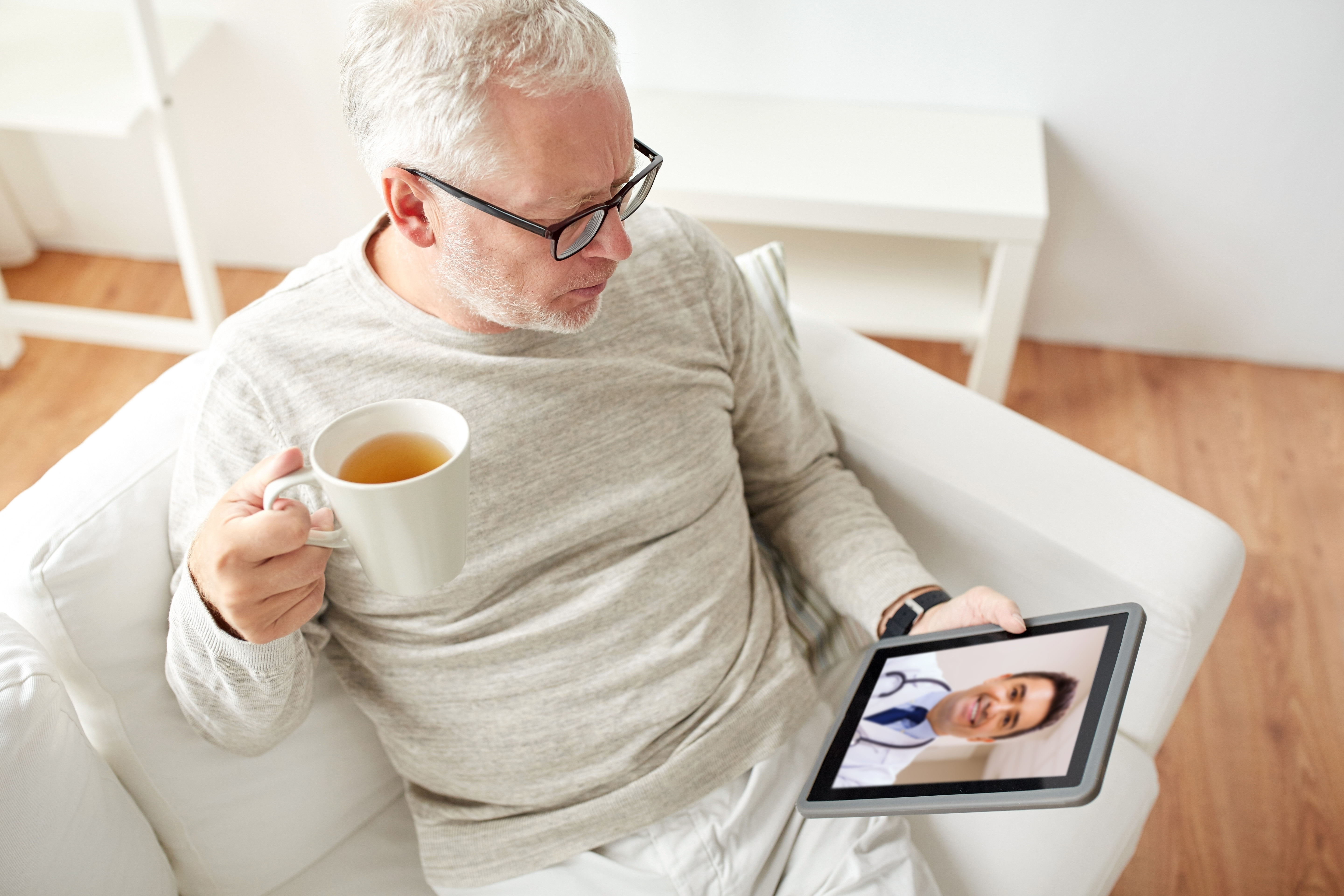 Man drinking a mug of tea and talking to doctor on tablet