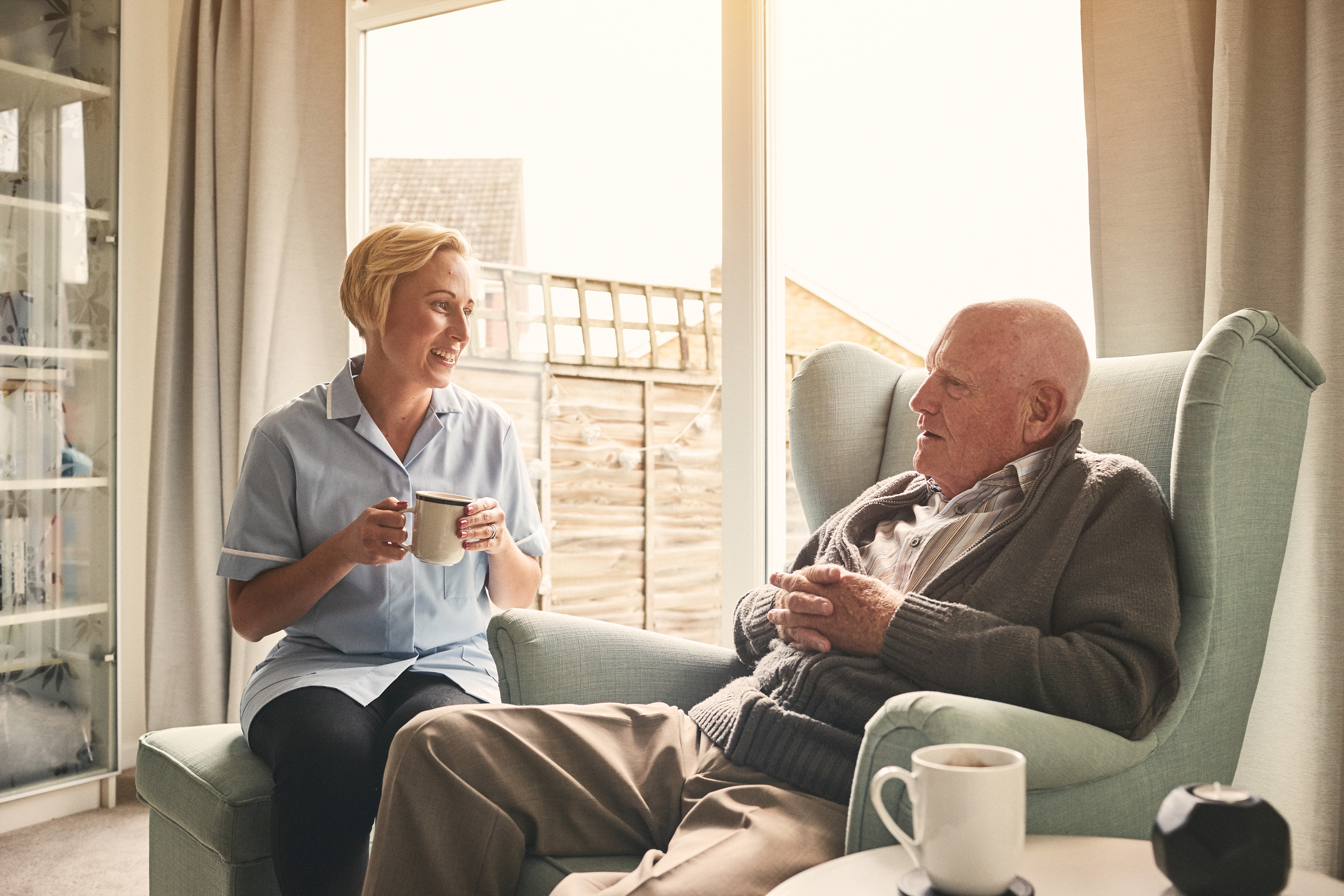 older white man drinking tea with nurse in his home