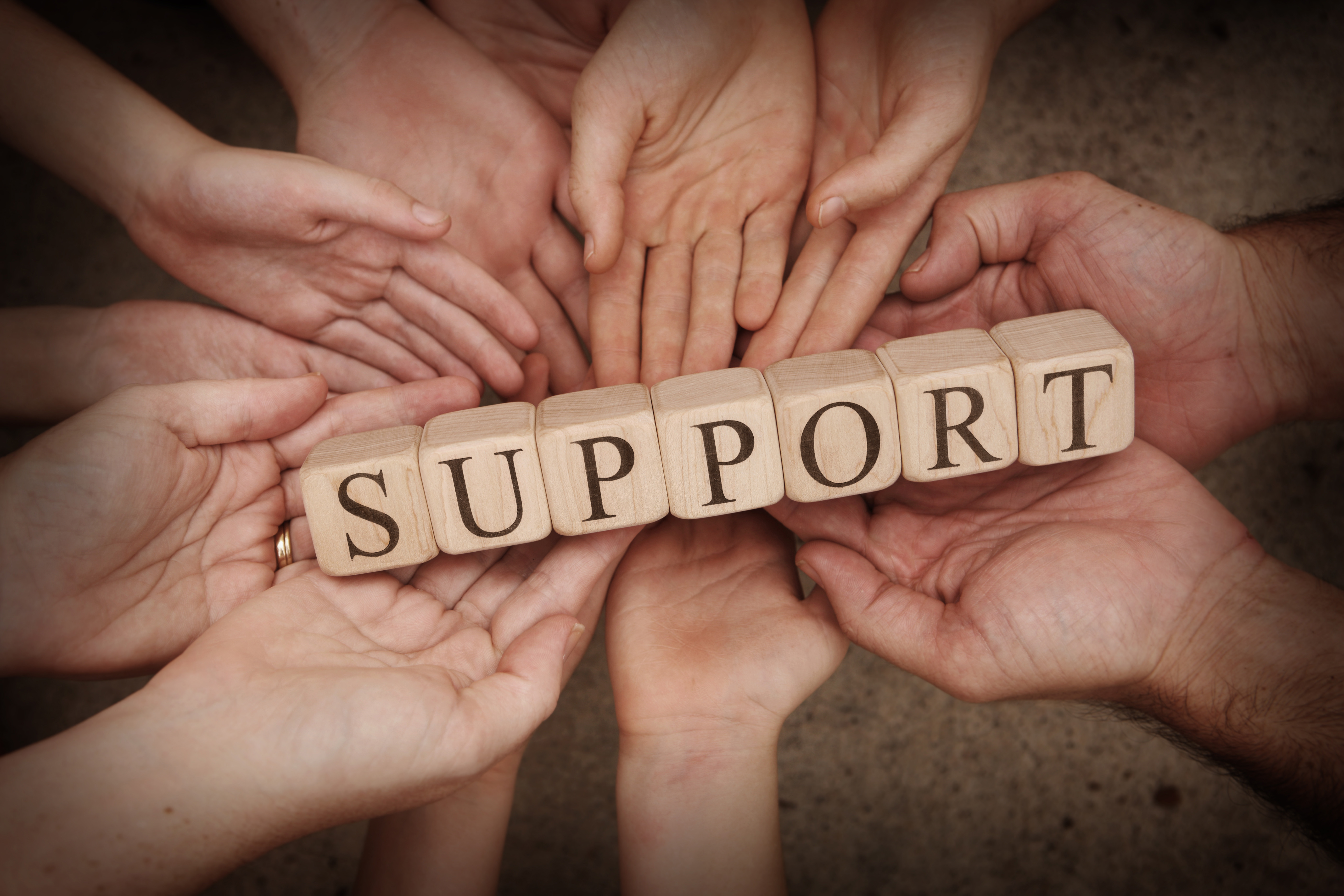 A group of hands holding blocks that spell out the word support