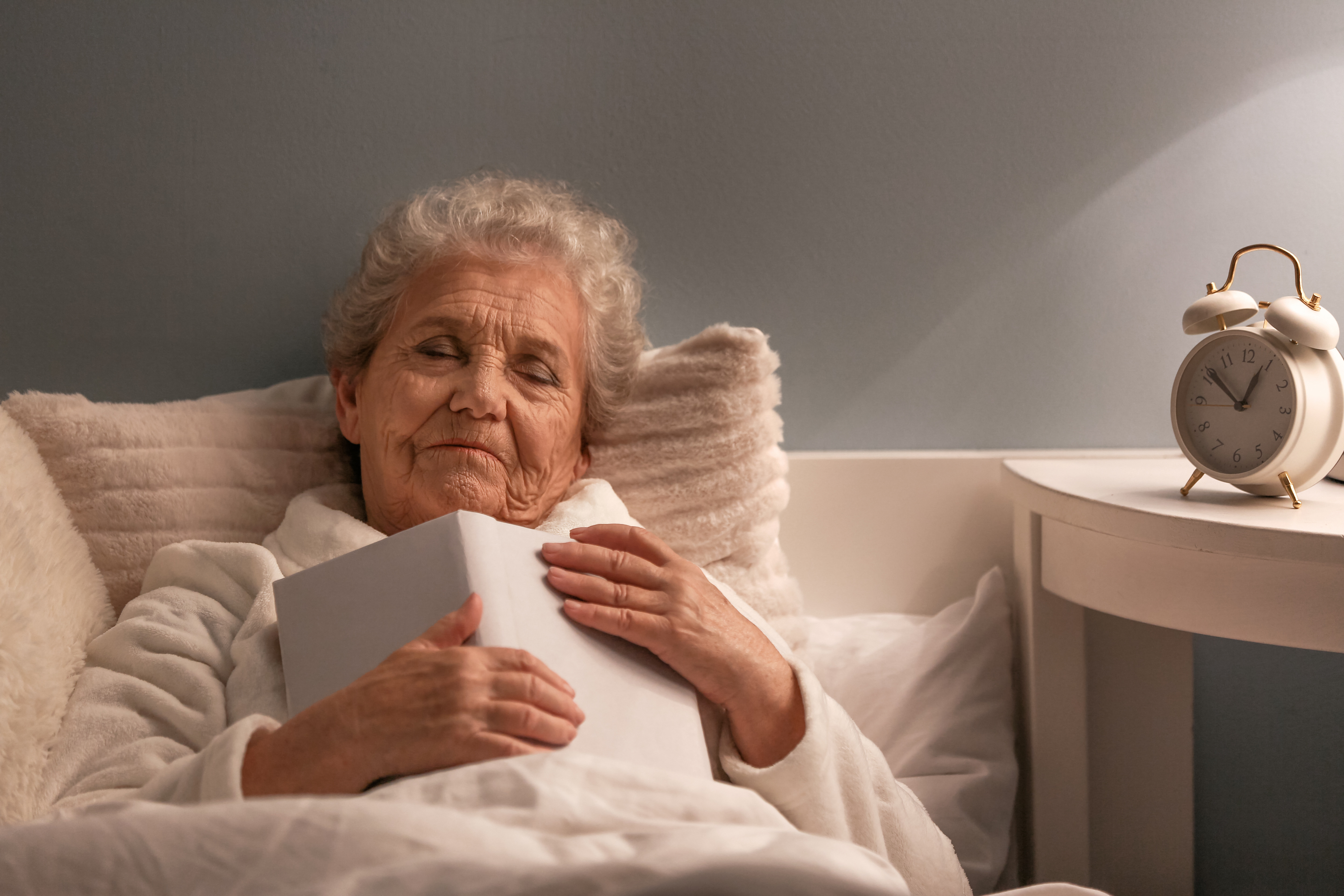 Older woman in bed asleep with open book on her chest
