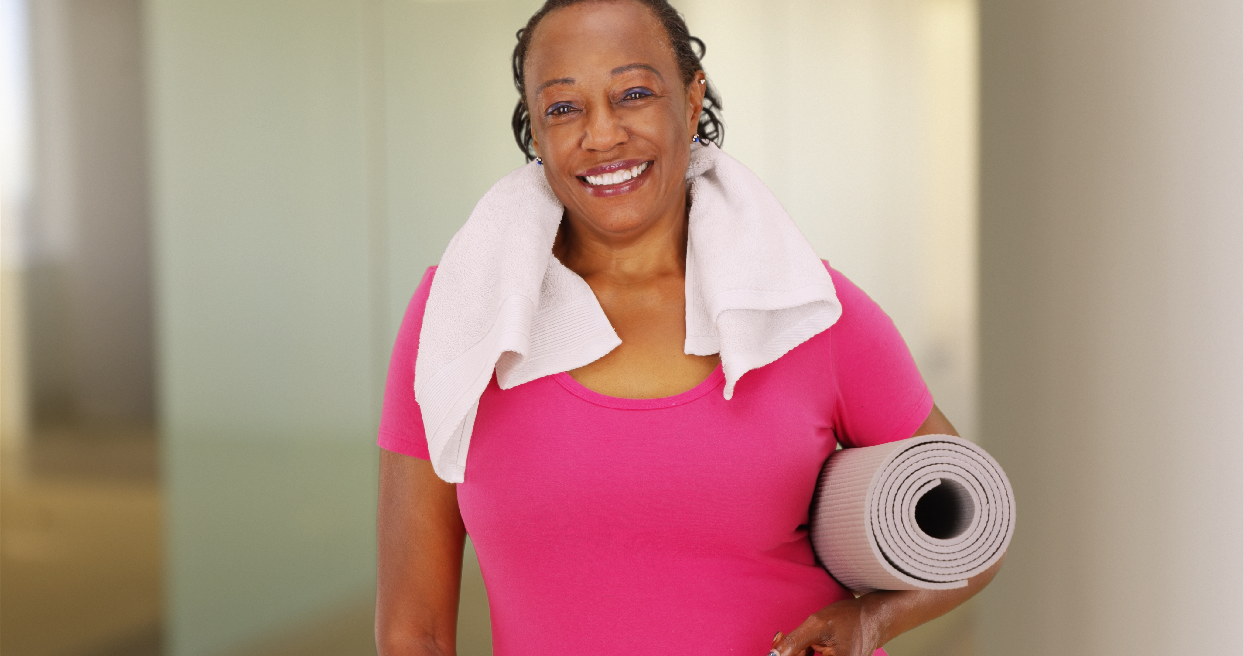 Lady at gymm with towel round her nexk and carrying a yoga mat