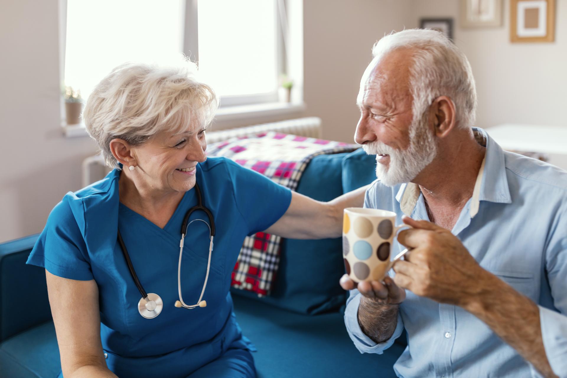 Older white man sittinh drinking tea with a nurse